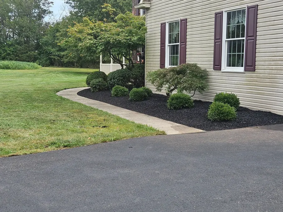 Freshly mulched landscape bed with trimmed shrubs along the side of a house